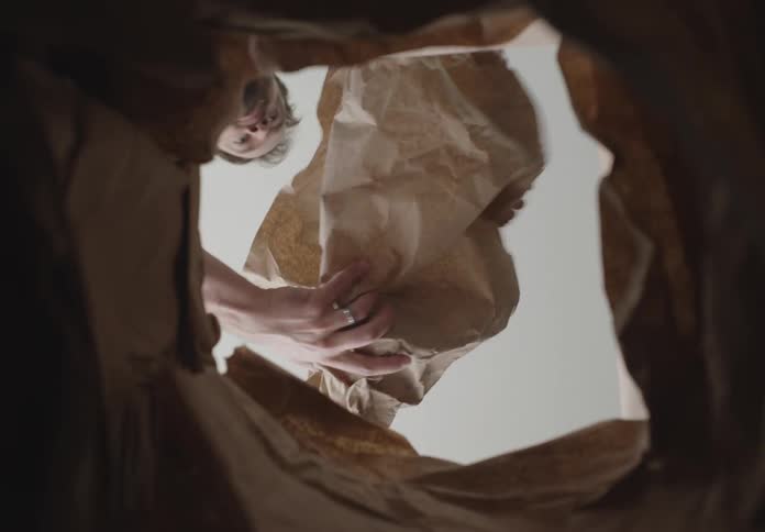 A young man takes a paper trash out of the waste bin and unfolds a white box from it
