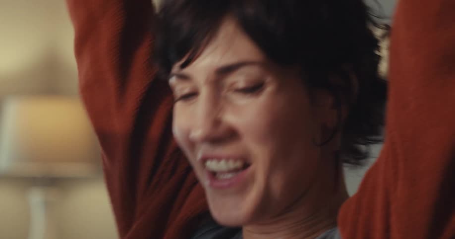 A woman takes off her glasses and raises her arms at the computer