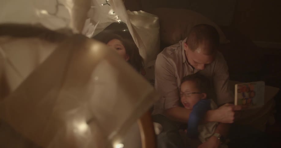 A man and children read a book under a blanket tent