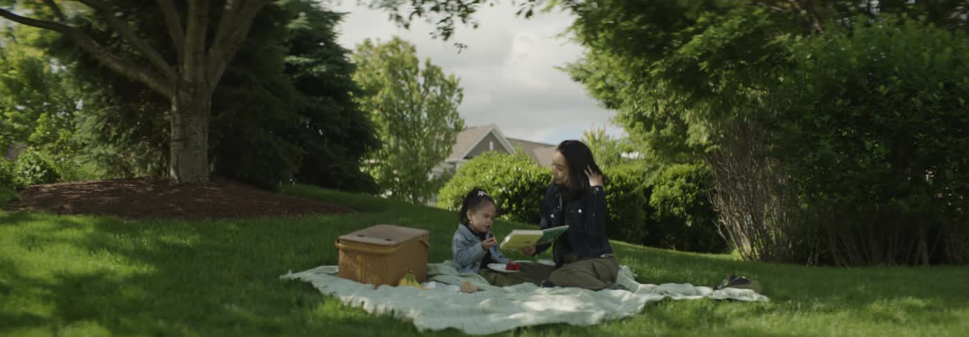Mother and daughter enjoy a picnic by reading a book on a field during the day