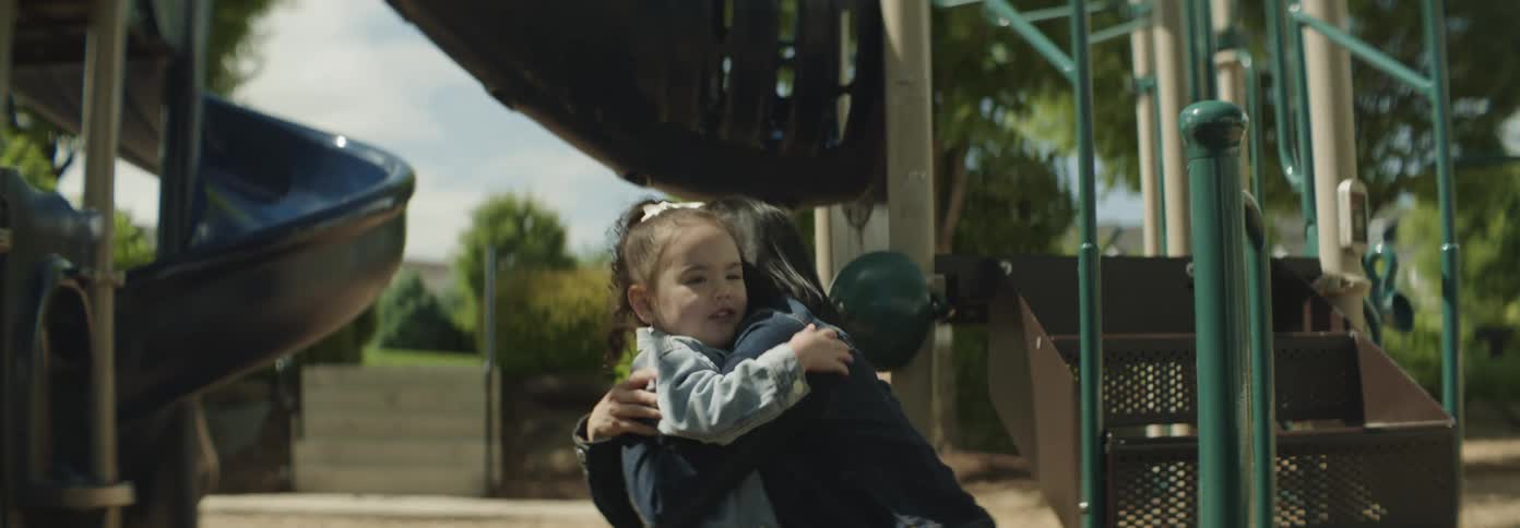 A girl child warmly hugs her mother in a playground