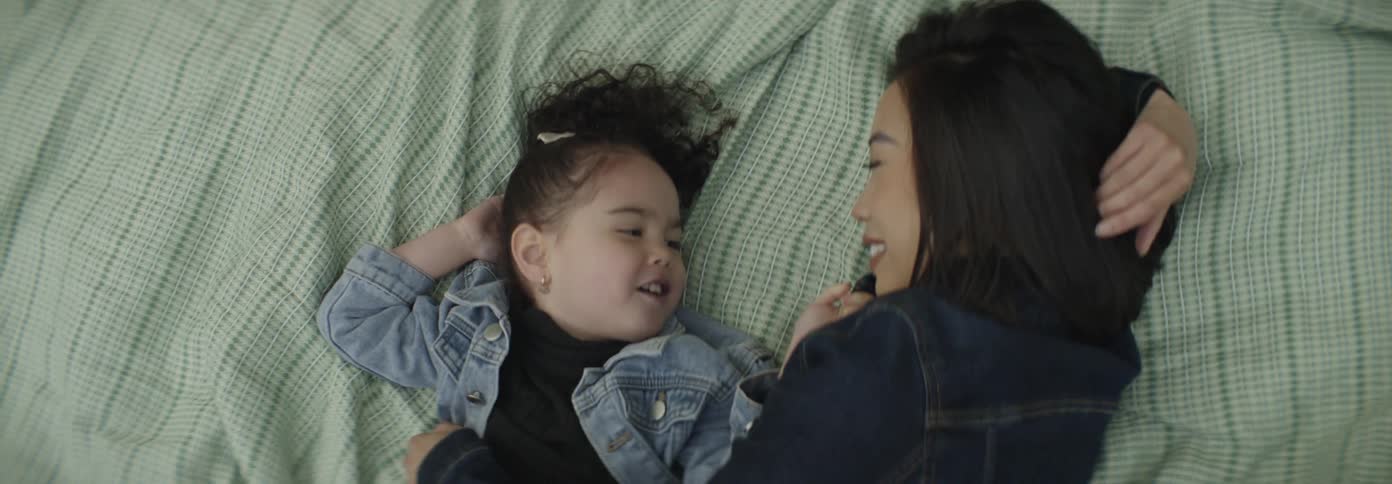 A mother and daughter lay on a blanket outside and bond together
