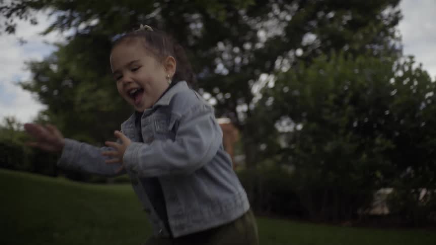 Mother blows bubbles in a sunny park while her young daughter joyfully chases and pops them