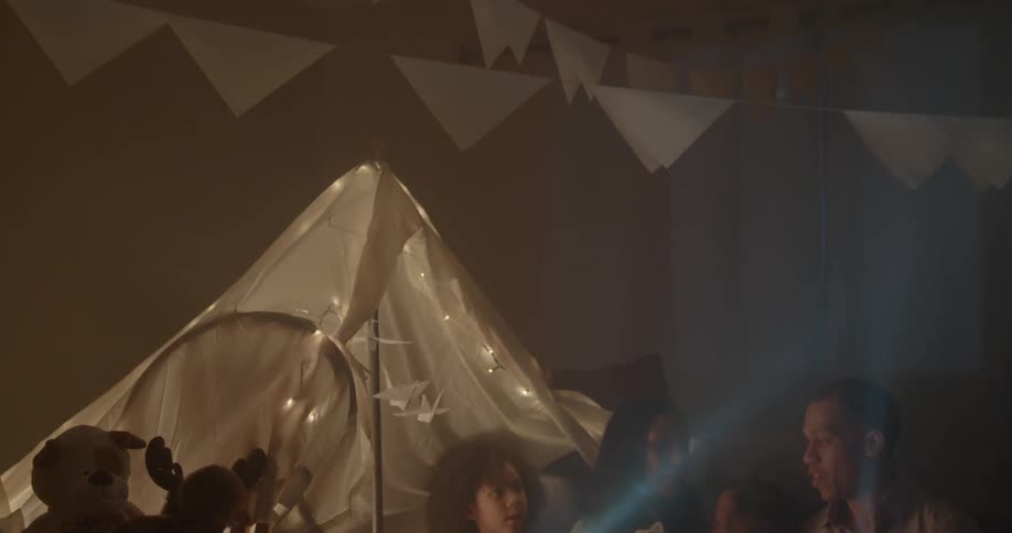 Group of people including children using flashlights to shine around indoors looking at things hanging on some lines