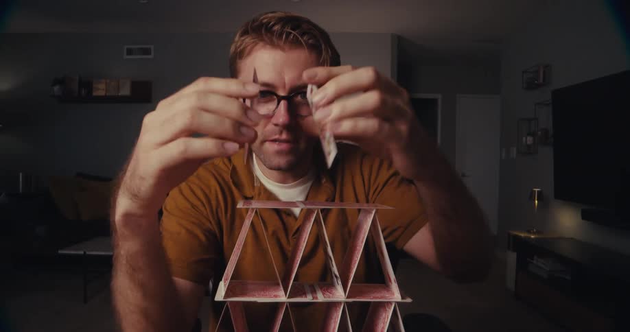 Timelapse of a man carefully building a pyramid out of playing cards in a cozy living room