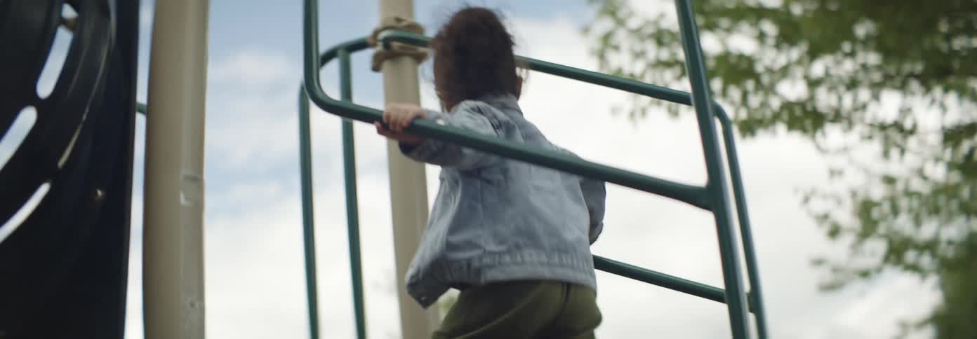 Mother and daughter climb the playground equipment in a residential area on a cloudy day