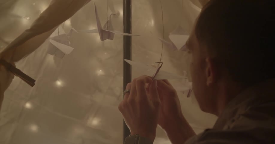 A man hangs origami birds inside a blanket tent
