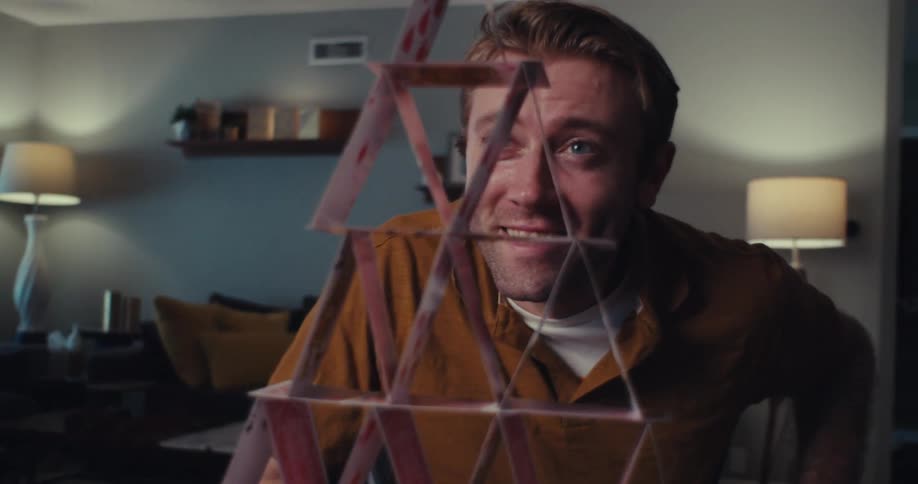 A man excitedly admires a pyramid he built using playing cards