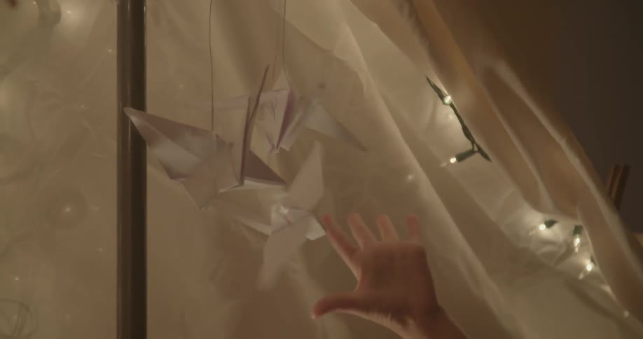 A child plays with origami birds in a blanket tent