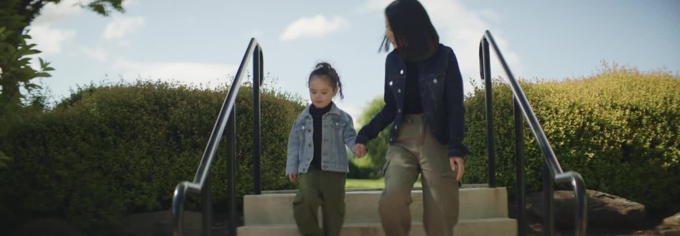 A woman walks down the stairs into a public park with her daughter on a sunny day
