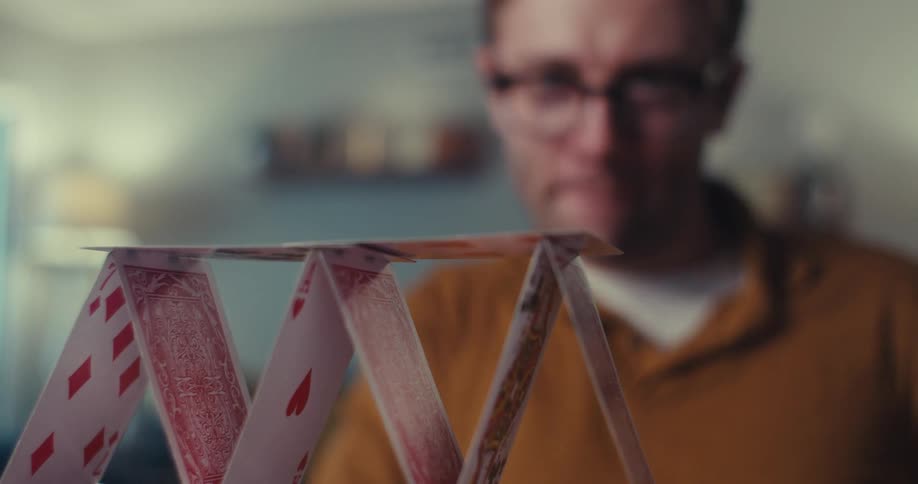 Man carefully building a playing card pyramid indoors with focus and concentration
