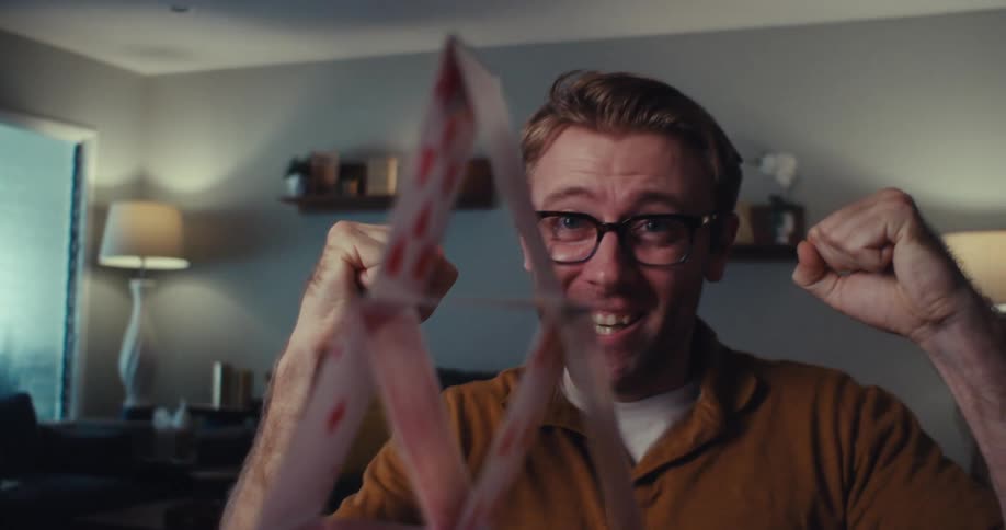 Close up of a man celebrating after carefully stacking cards in a triangular pattern in a room
