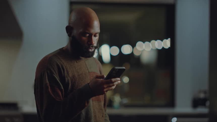 A man is standing inside looking at his cellphone