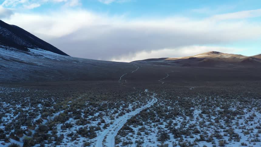 A winding trail crosses a snowdusted valley surrounded by mountains under a clear sky