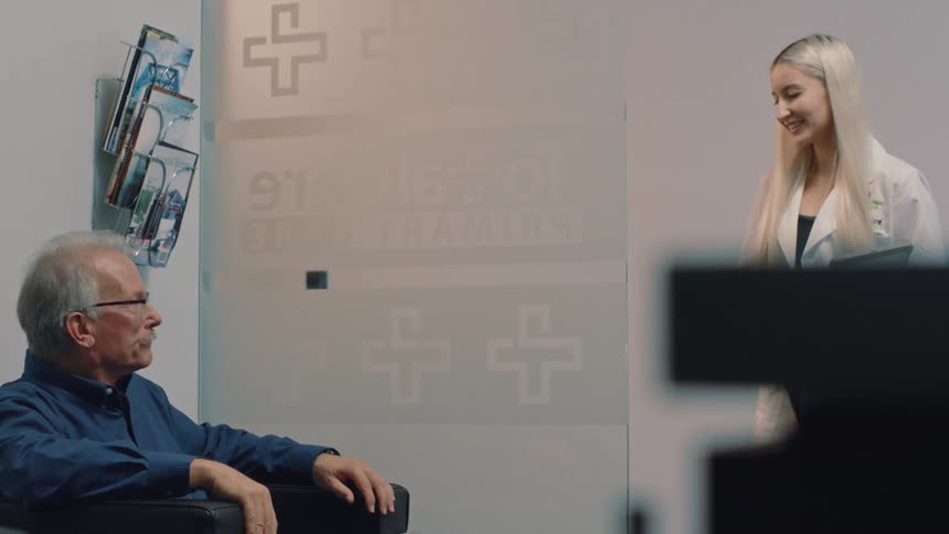 Female doctor calls an elderly man in for his appointment from a waiting room in a hospital