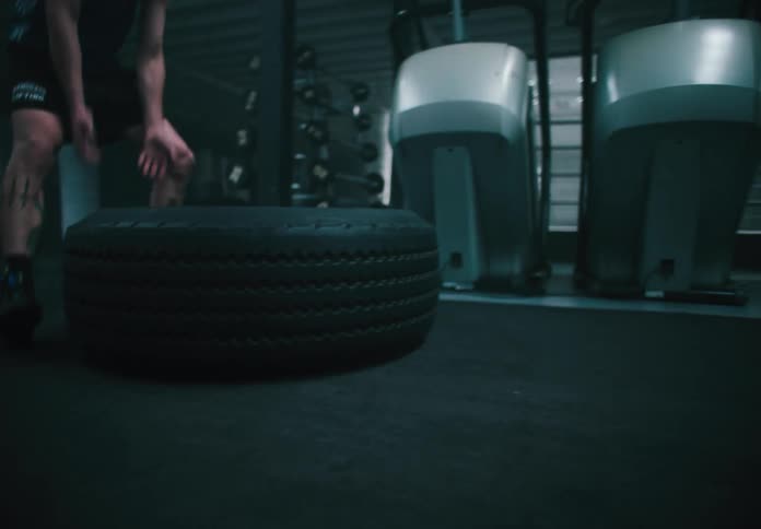 A man is flipping a large tire in a gritty indoor gym environment