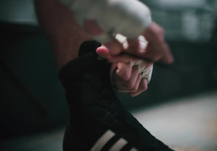 A boxer in the gym wearing wrist wraps laces their shoe while getting ready for training
