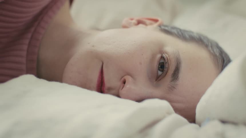 A discouraged woman lies on a bed staring ahead with no reaction