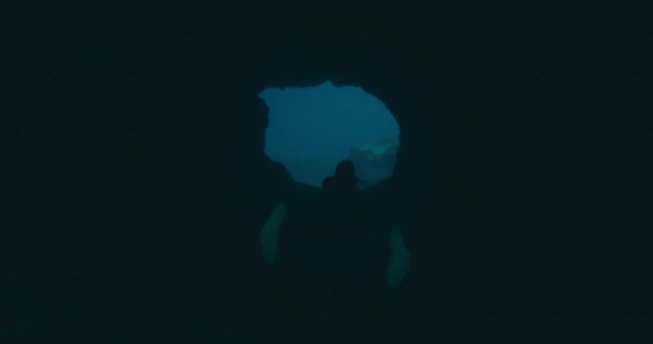A woman swimming underwater through a tunnel of coral