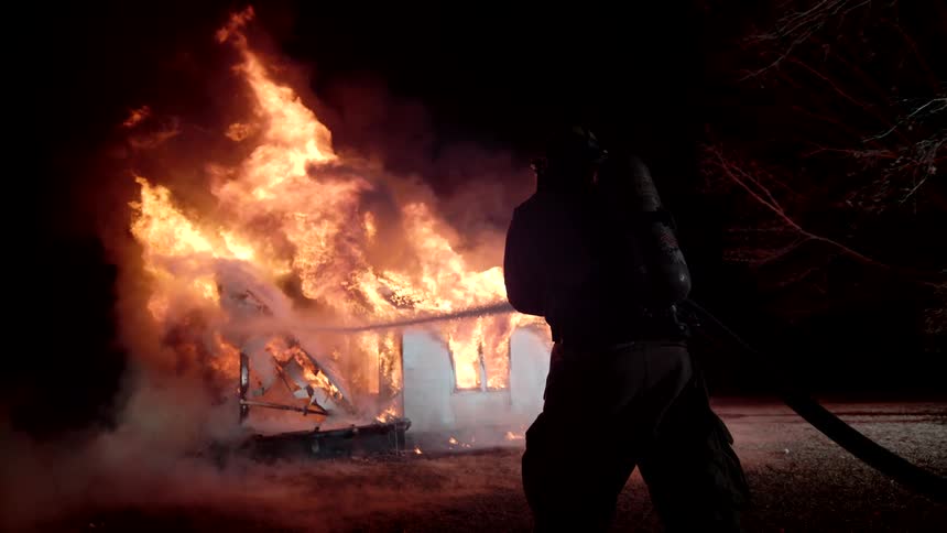 Firefighters direct water at a blazing house fire at night