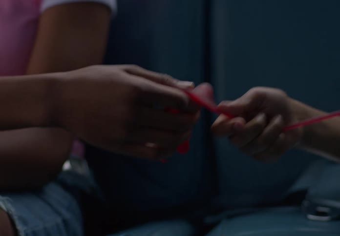 Two children sit in the back of a car quietly playing with a red stretchy toy