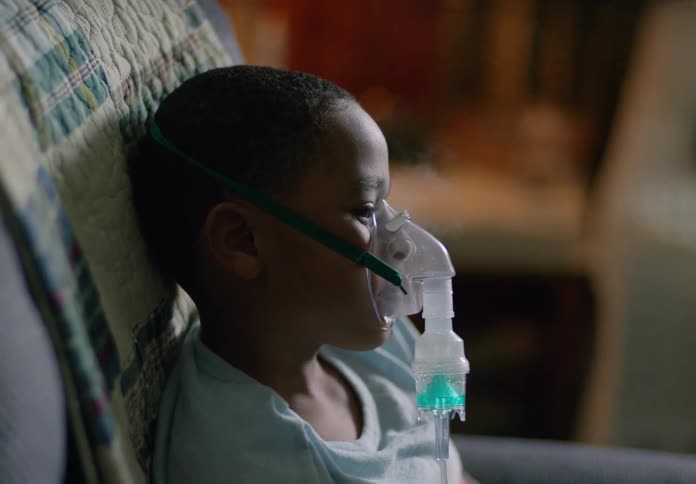 Boy receives a breathing treatment via a nebulizer while sitting leaning against a quilt