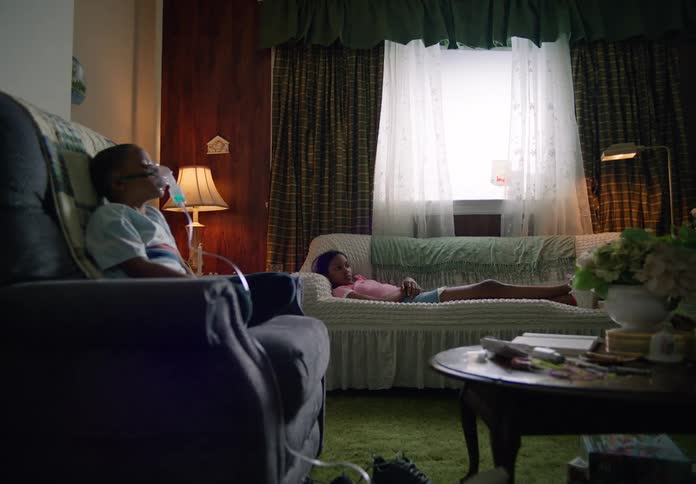 Son receives a nebulizer treatment and his sister lies on the couch while their father talks on a phone