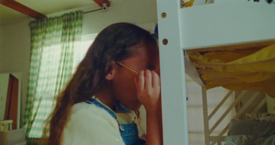 A young girl wearing glasses hides her face on the side of a bunk bed playfully calling out for a game of hide and seek