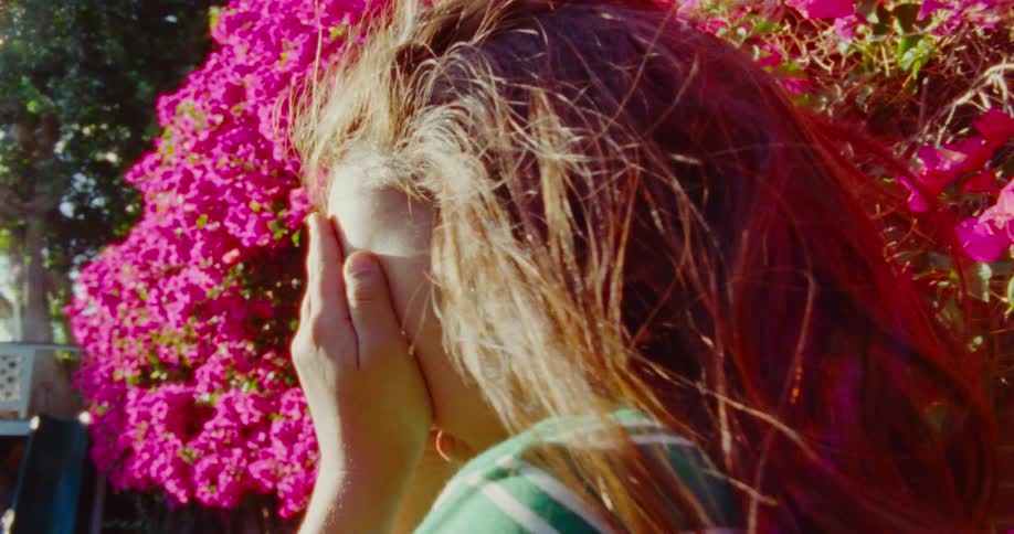 A little girl counts with her hands over her eyes near a bougainvillea plant