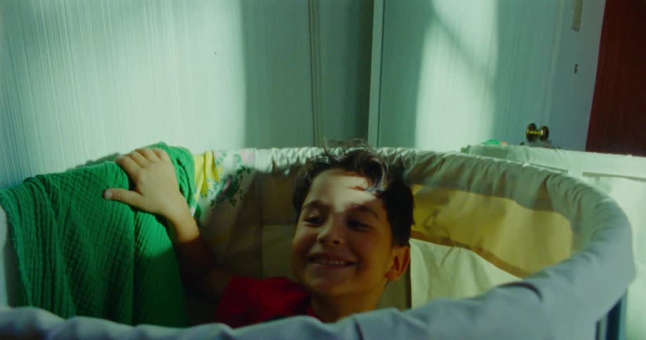 A little boy surprisingly pops up from inside of a laundry basket while smiling