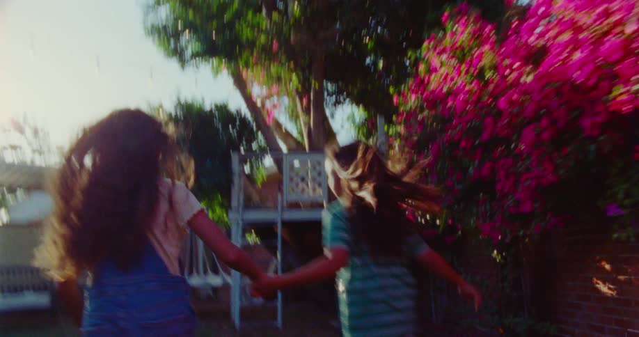 Two little girls are holding hands while excitedly running around a back yard