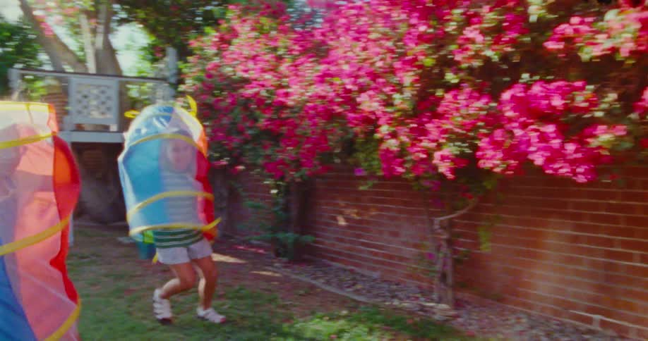 Two children with plastic toys on their bodies running through the backyard of a house during the day