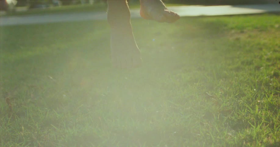 Bare feet dangle in the bright sunlight against a backdrop of trees and a lawn