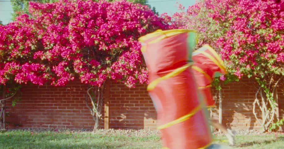 Two children with plastic toys on their bodies running through a yard with pink flowering trees in the background