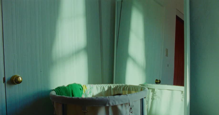 A young male child plays by hiding inside a laundry basket positioned beside a mirror