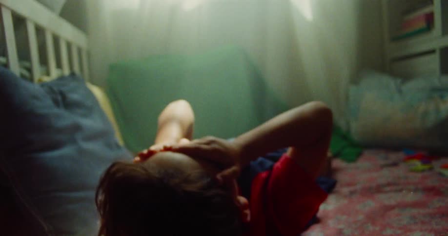 A kid lies alone on a bed at midday covering her eyes