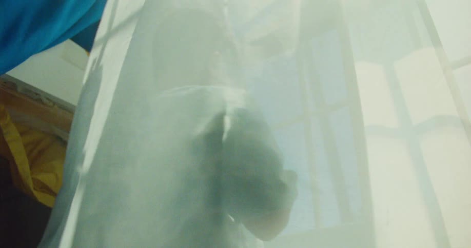 Two barefoot children run across a patterned rug in a room reach the window and wrap themselves in curtains while spinning