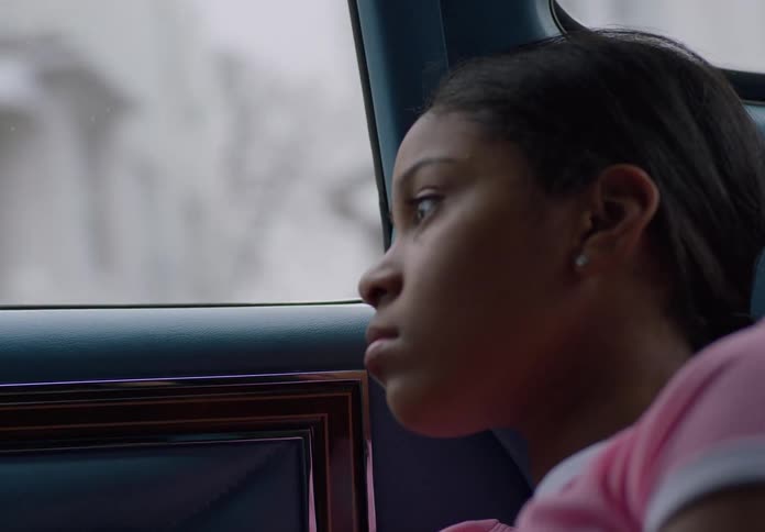 A sad little girl gazes out the window of a moving car