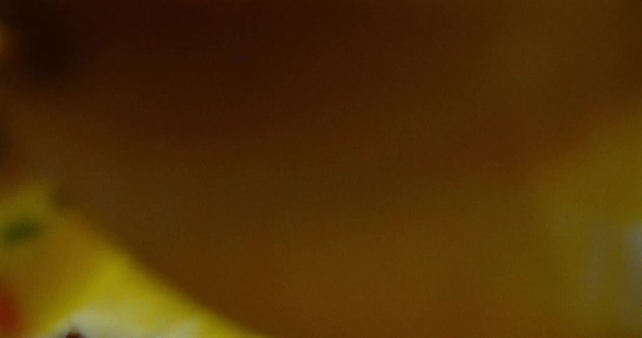 A boy playfully shakes a yellow and white blanket over the camera in a sunlit room