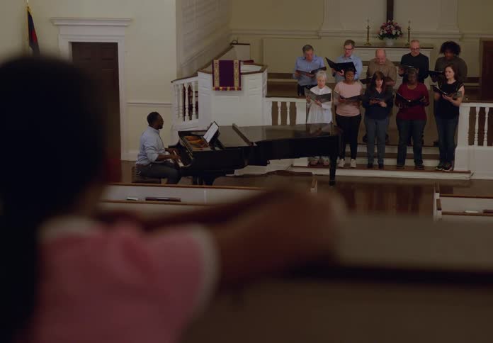 A choir sings in a church as a child watches from a pew