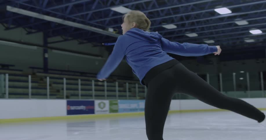 Woman spinning on one leg on ice skates on indoor ice rink
