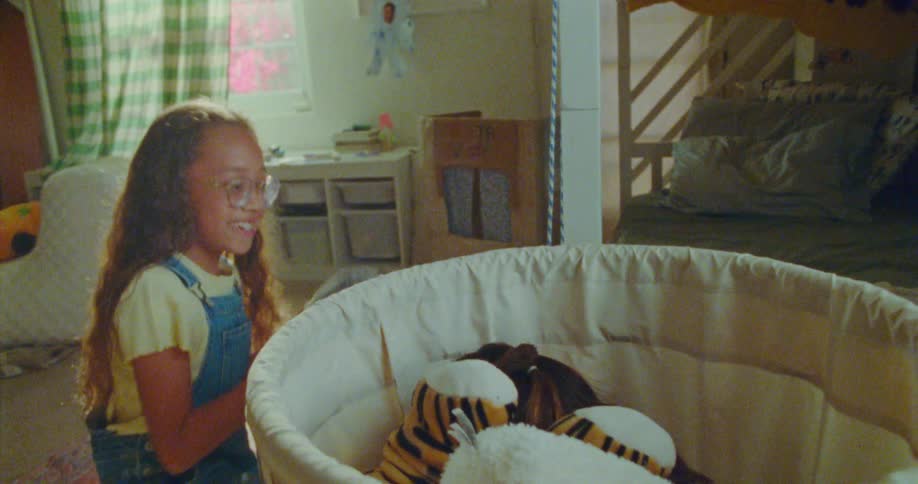 Two girls play hide and seek in a sunny room one hides in a clothes hamper while the other covers her with toys and a blanket