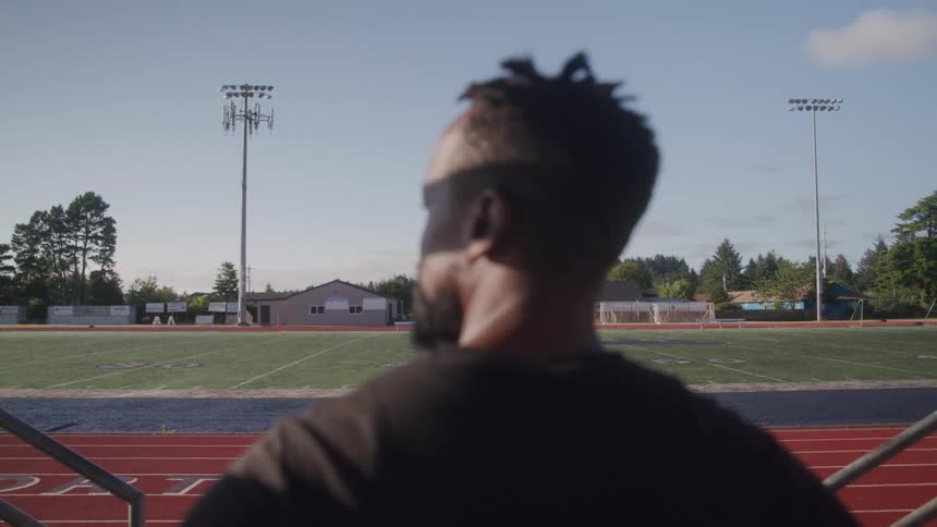 A man stands and stares at a football field at midday