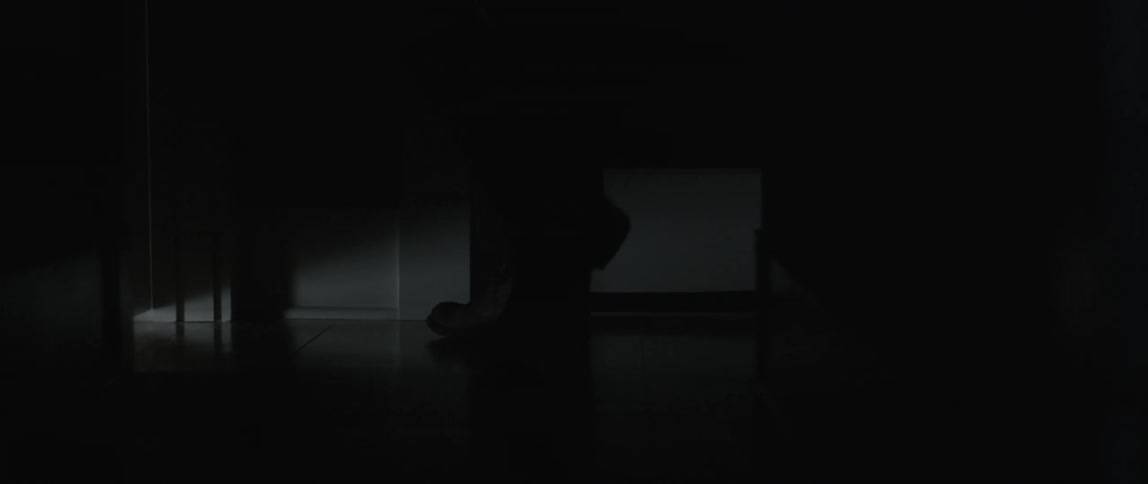A person walks to the door of a dark room and exits