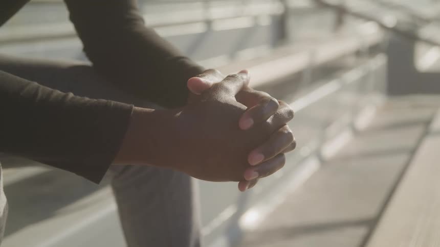A man is sitting on the bleachers with her hands folded