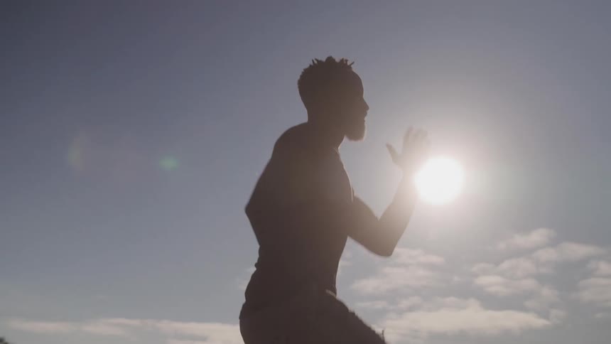 The silhouette of a man stretching his legs outdoors with sunlight behind him