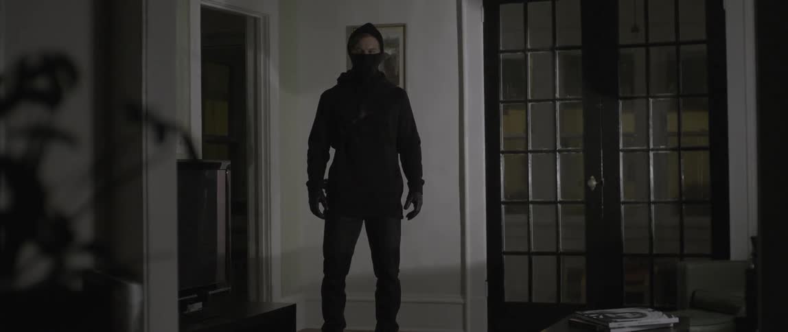 Masked burglar walking into a darkened room as lights shine on him from a passing vehicle