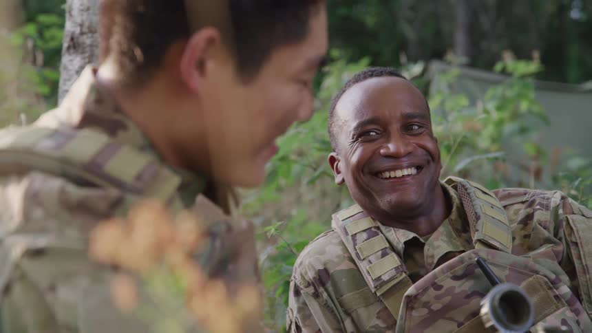 Two soldiers sitting in a makeshift camp talking smiling