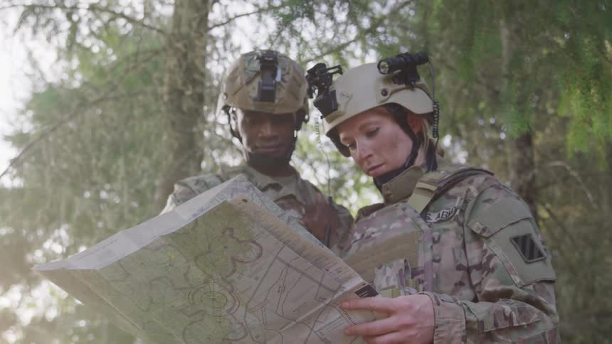 The faces of two soldiers in military gear who are standing there staring at a map held in the hand of one of them