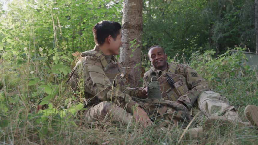 Two soldiers sit in the grass talking